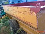 un camion-benne jaune avec un toit rouge, garé dans une cour