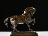 statue en bronze représentant un cheval, posée sur un socle en bois, sur fond noir