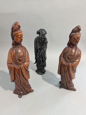 trois figurines en bois représentant des personnages asiatiques, posées sur un fond blanc