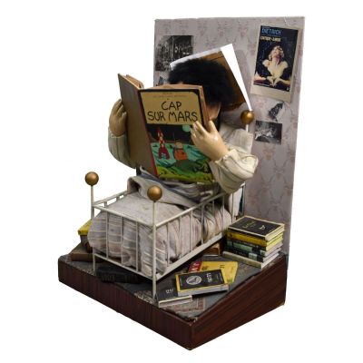 une figurine représentant une femme en train de lire un livre, posée sur un lit