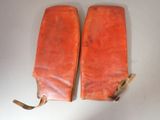 pair of orange leather gloves on a white surface with a brown cord