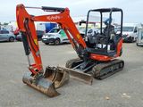une pelleteuse orange garée sur un parking, avec d'autres véhicules en arrière-plan