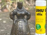 une petite statuette représentant une femme, à côté d'un tube d'Uhu Stix