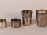 three silver cups and a silver napkin on a white surface