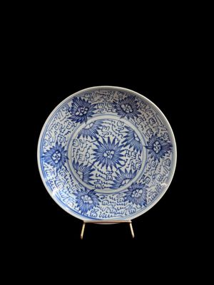 une vieille assiette bleue et blanche posée sur un socle, sur fond noir