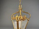 a brass hanging light fixture with glass panels and a chain