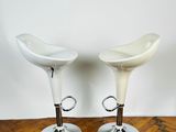 two white stools sitting on top of a wooden floor next to a white wall