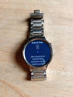 une montre connectée posée sur une table en bois, avec un écran bleu