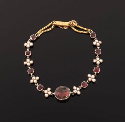a gold bracelet with garnets and pearls on a black background