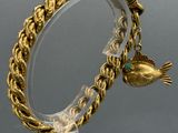 a gold bracelet with a bird on it on a clear stand