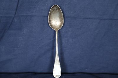cuillère plaquée argent posée sur un tissu bleu avec un fond noir