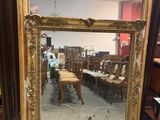 an antique gold framed mirror with a chair and a table in the background