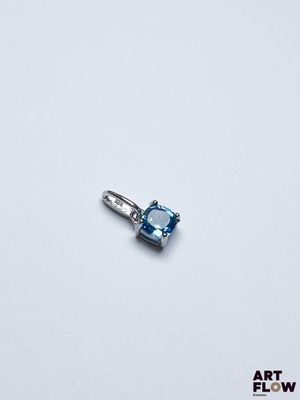 une image représentant un pendentif composé d'une topaze bleue et de diamants, posé sur une surface blanche