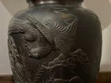 a black vase with a bird on it sitting on a table