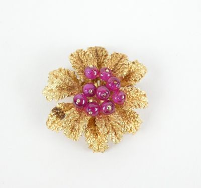 broche en forme de fleur violette et dorée, ornée de perles, sur fond blanc