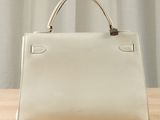 a white purse sitting on top of a wooden table next to a curtain