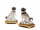 une paire de figurines représentant un carlin et un chat, posées sur un coussin