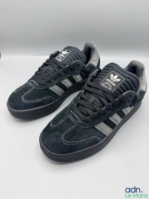 Les baskets adidas sont noires et grises, avec une bande argentée.