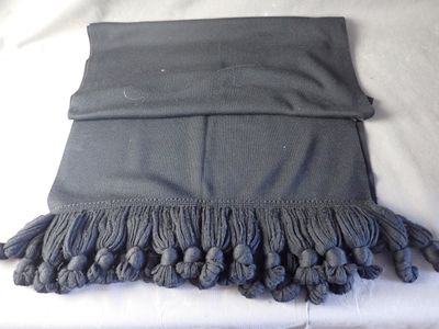 a black scarf with tassels on it on a bed