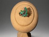 a ring with a green stone on it on a stand