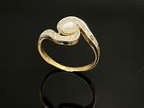 un gros plan d'une bague en or sertie d'une perle, posée sur une surface noire