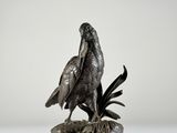 une statue en bronze représentant un oiseau posé sur un rocher, sur fond blanc