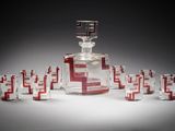 une carafe en verre, devant laquelle se trouvent plusieurs verres à shot