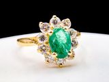 a close up of a green emerald and diamond ring on a white plate
