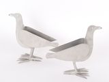 two metal birds standing next to each other on a white surface