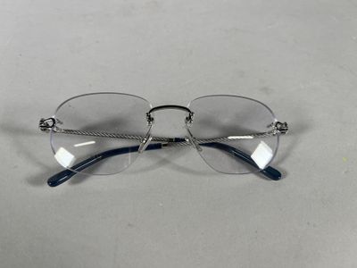 des lunettes posées sur une surface blanche, avec une chaîne autour de la monture