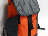 un sac à dos orange et gris posé contre un mur, sur une surface blanche