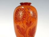 un vase orange orné de fleurs, posé sur une surface blanche