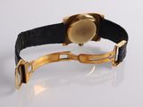 a gold watch on a black leather strap on a white surface