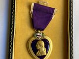 une médaille violette en forme de cœur, dans un écrin doré, entourée d'un ruban violet