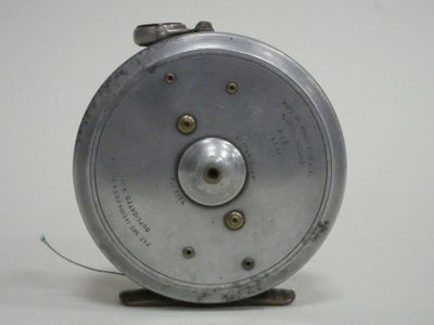 a silver fishing reel that is on a white surface