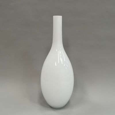 un vase blanc posé sur une table, sur fond gris