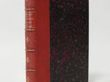 an old book with a red cover sitting on top of a white surface