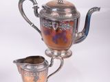 a silver tea pot and a silver cup on a white surface