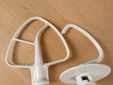 two white mixer attachments sitting on a wooden table