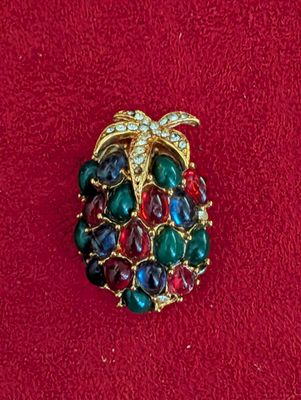 une image représentant une broche ornée de pierres multicolores sur un fond rouge