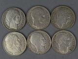 six silver coins of different sizes and shapes on a gray surface