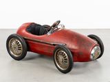 une vieille petite voiture rouge posée sur un sol en béton