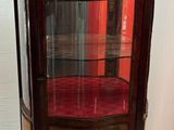 une vitrine avec une porte vitrée, placée dans un coin