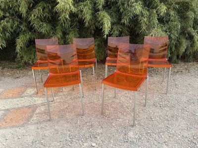 four orange plastic chairs sitting on top of a gravel ground
