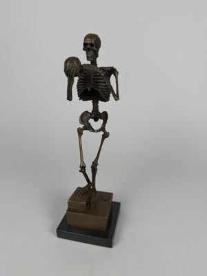a bronze statue of a skeleton holding a human skull on a wooden base