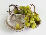 a silver plate with grapes in it on a white surface