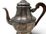 an old silver teapot with a wooden handle on a white surface