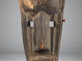 a close up of a wooden mask on a stand on a white surface