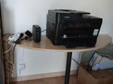 a black printer sitting on a small table next to a refrigerator