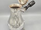 an antique silver plated coffee pot with a handle on a stand